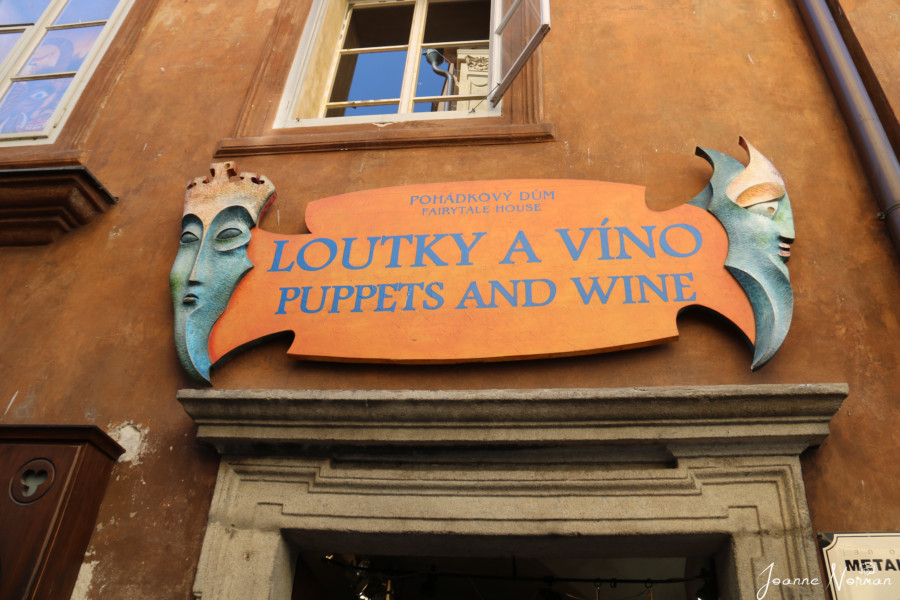 orange wooden store sign with green puppets on each side stating puppets and Wine 