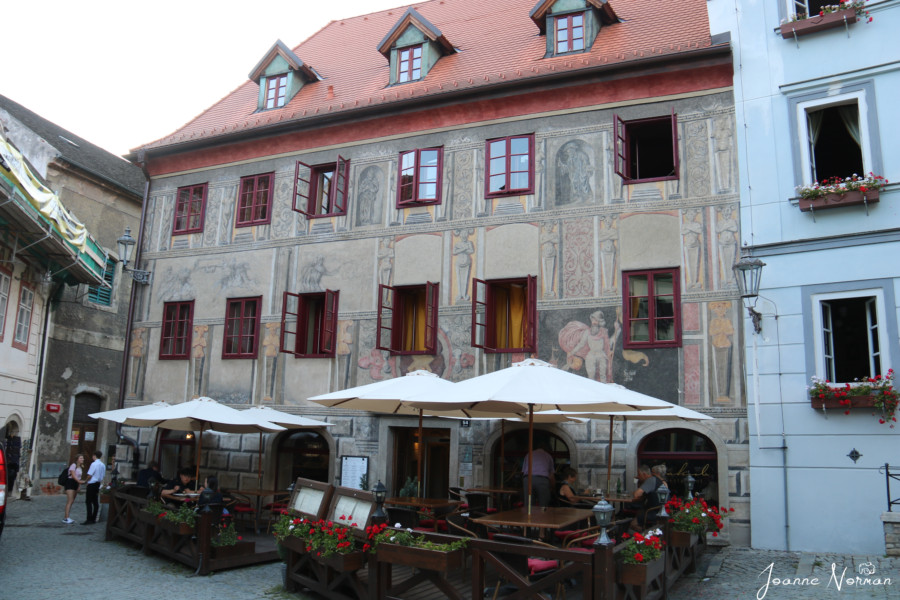 square building with many windows and frescos on the walls with outdoor seating is Jakub restaurant cesky krumlov