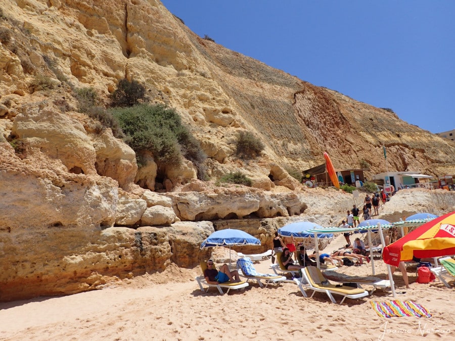 family sitting on sunbeds with umbrellas and cliffs behind Praia de Vale Centeanes