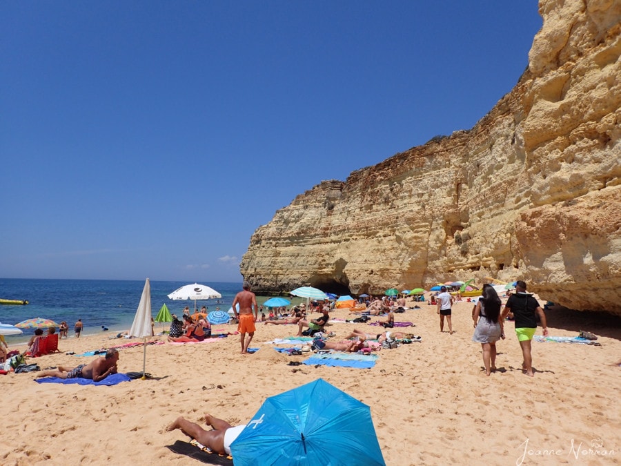 large sandy beach with orange cliffs on one side and blue ocean on other Praia de Vale Centeanes