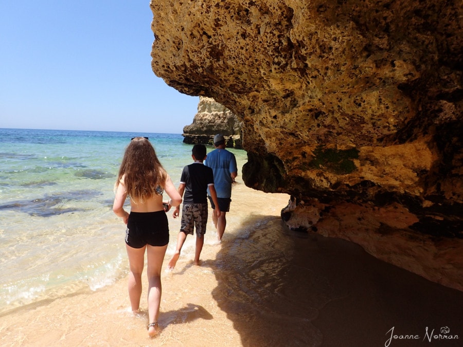 John, Caiden and Sydney walking under cliff overhang on beach towards cave
