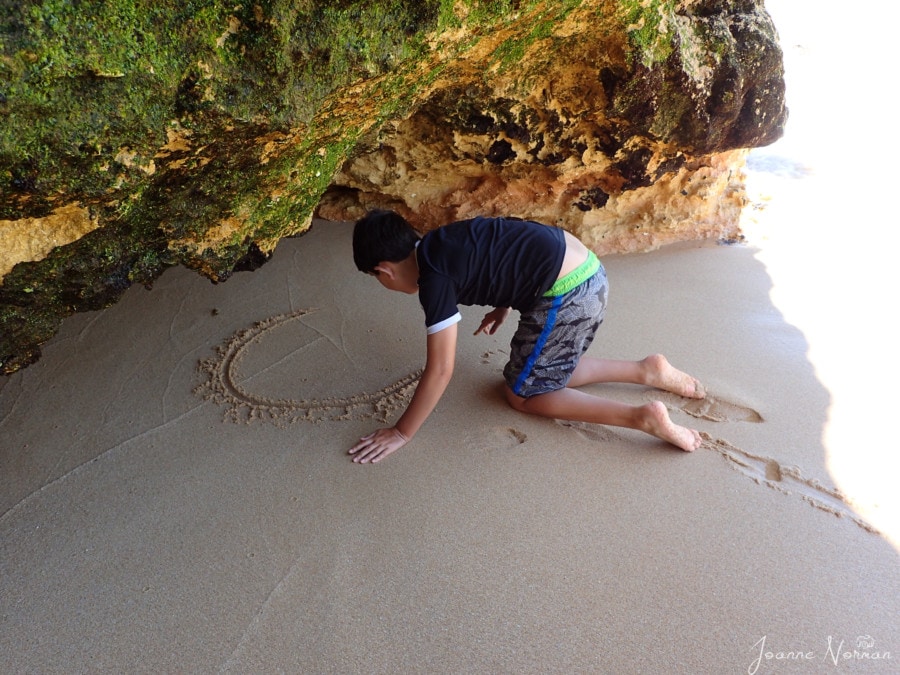 Caiden writing his name in the sand inside cave
