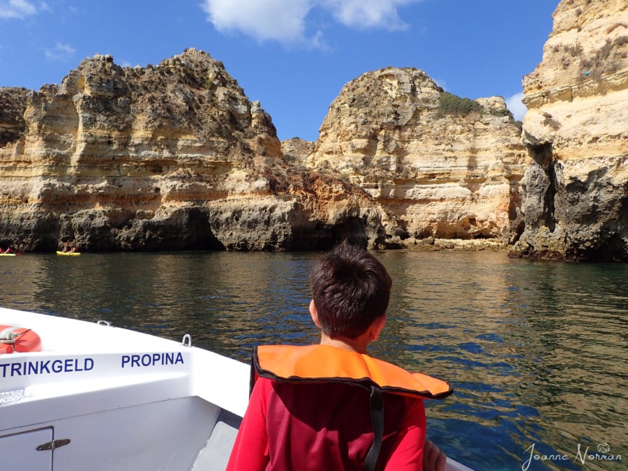 caiden in red shirt on side of boat looking at sandstone cliffs and rock formations