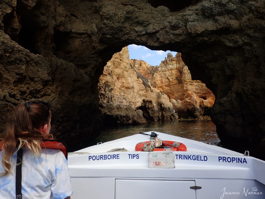 tip of white boat with Sydney sitting in front going through archway in massive limestone rocks  Ponta da Piedade Lagos from Carvoeiro