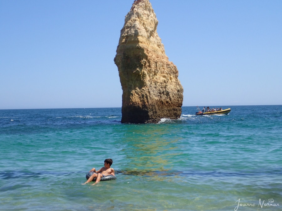 Caiden floating in grey tube in front of rock formation at Praia do Carvahlo