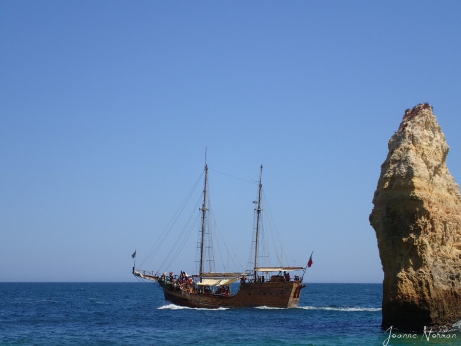 pirate ship floating past rock formations in ocean at Praia do Carvalho