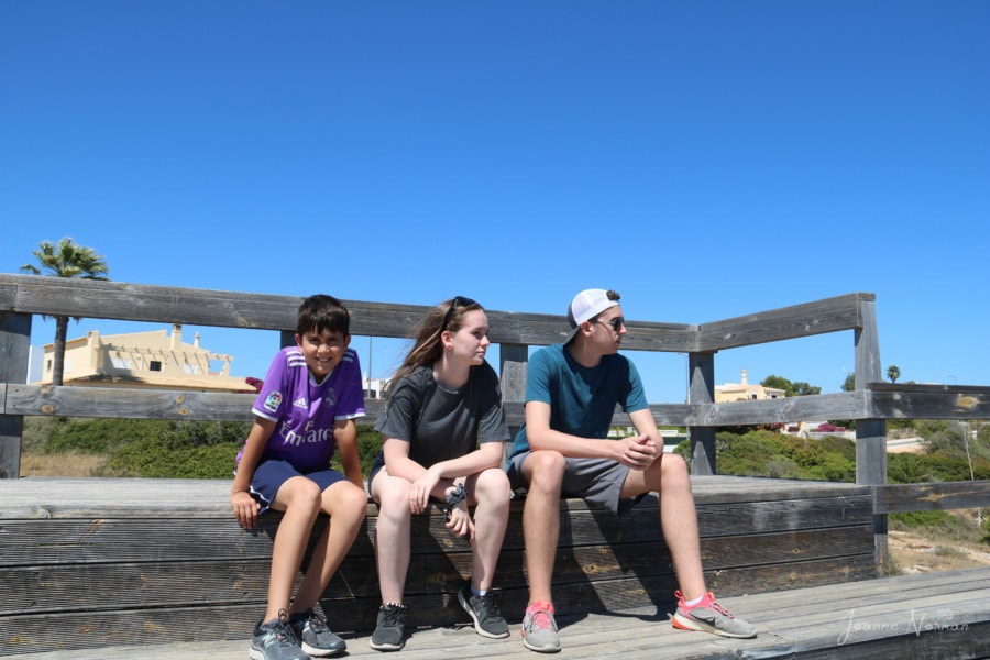 three kids sitting on bench looking out over ocean is things to do in Carvoeiro boardwalk