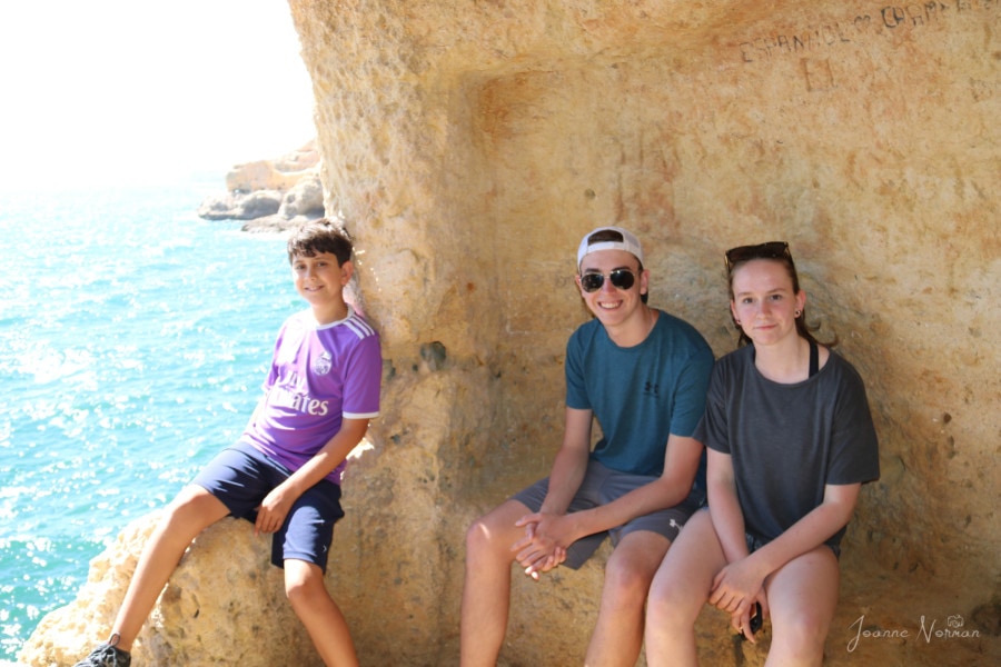 three kids sitting on stone bench inside cave with hole open to ocean