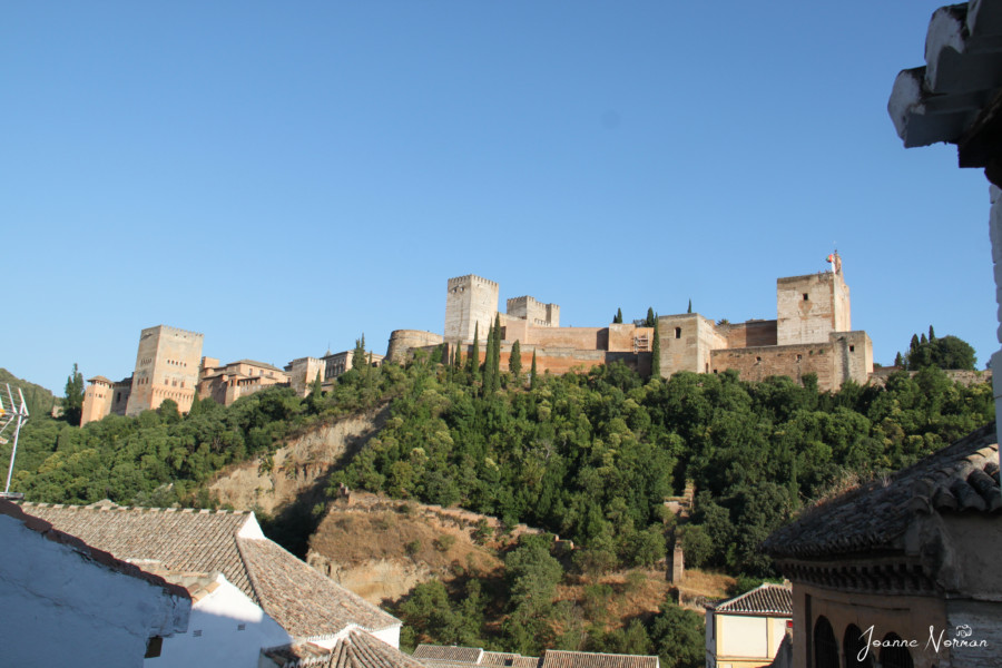 Alhambra from a distance looks like a castle on a hill of green trees spain itinerary
