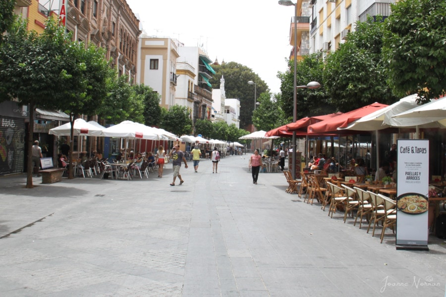 street with small bistros with tables and umbrellas lining each side in Triana Seville