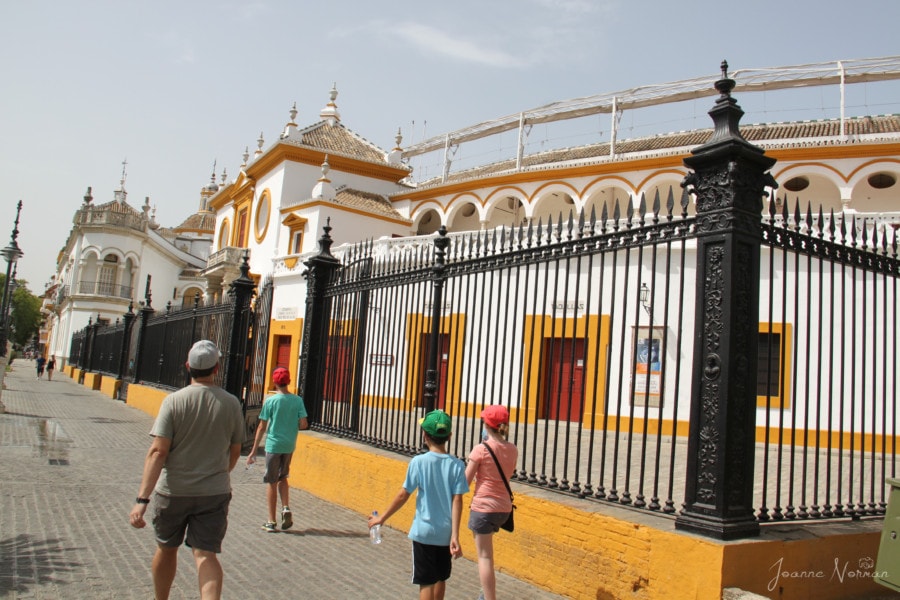 family wandering a street in front of white building with yellow trim which is bullring Seville