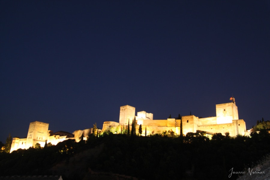 distant nighttime view of the Alhambra palace glowing on a hill