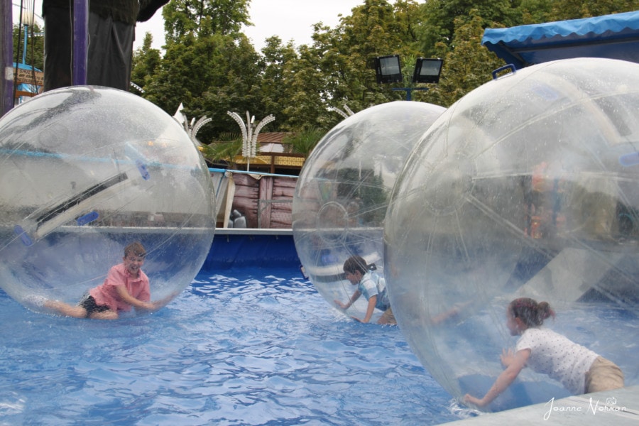 three large clear balls with a child inside each one rolling on water
