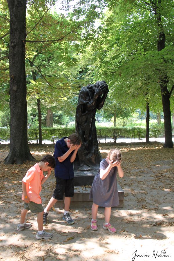 three kids recreating statue behind holding its head