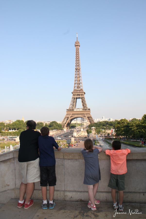 three kids and dad leaning on fence watching Eiffel Tower in distance