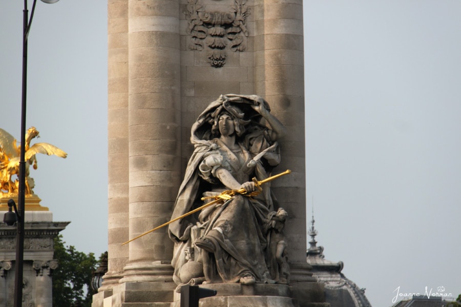 stone pillar of bridge with woman holding gold sword