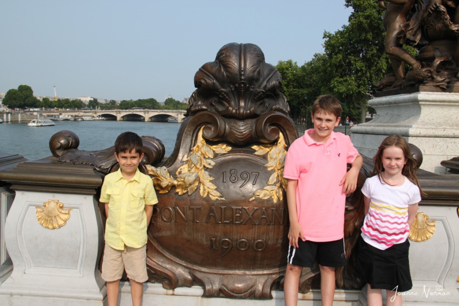 3 kids standing in front of Pont Alexandra brass sign