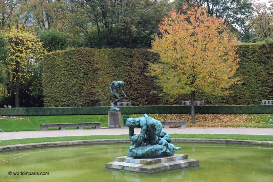 green statue of man on knees with head down with yellow trees behind is autumn in Paris France